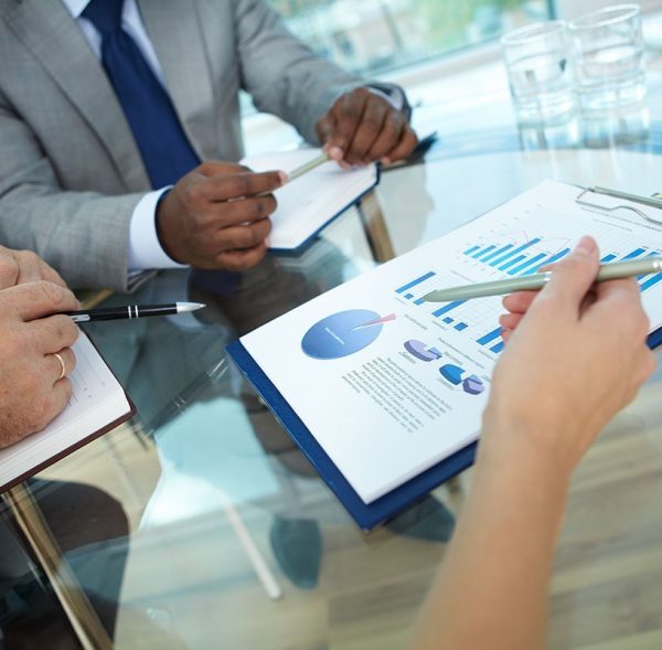Close-up of human hand with pen pointing at paper while explaining something to colleagues