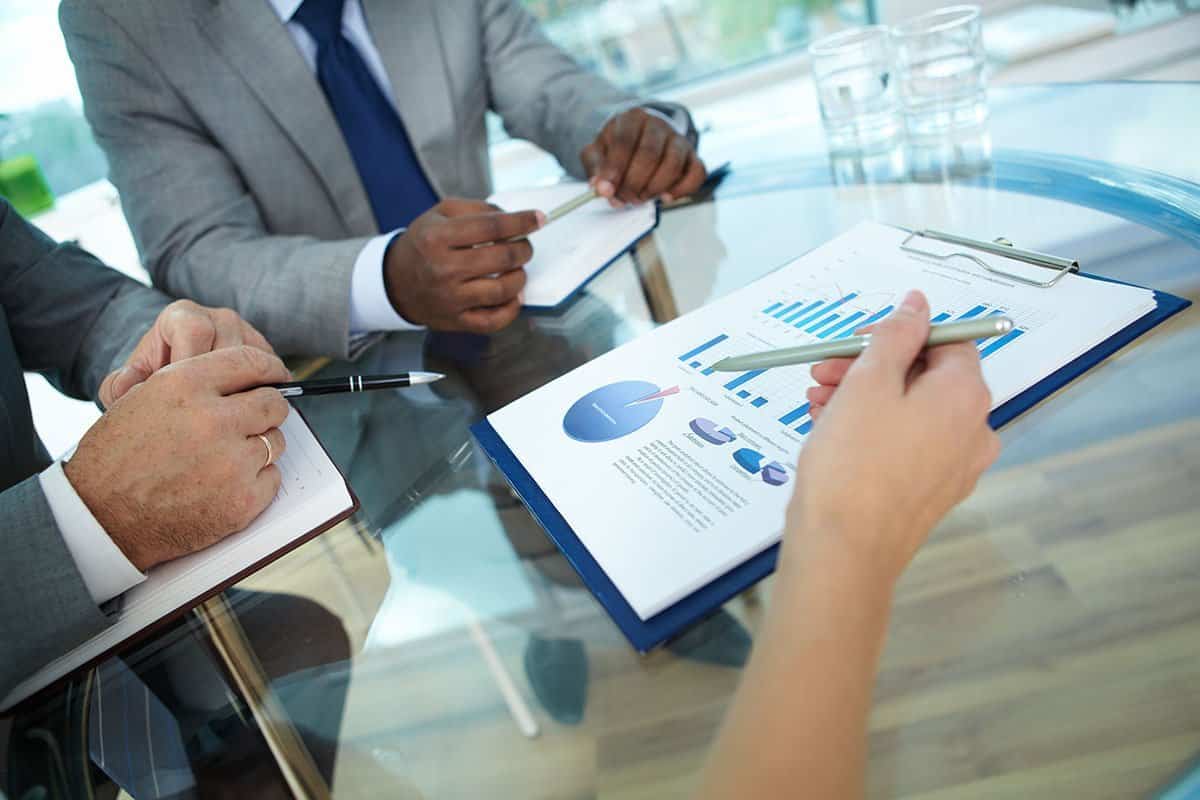 Close-up of human hand with pen pointing at paper while explaining something to colleagues